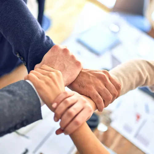 Colleagues clasping hands over a desk — adopting AI together, as a team